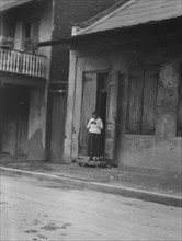 View from across street of a woman standing in a doorway in the French Quarter, New..., c1920-c1926. Creator: Arnold Genthe.