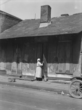 View from across street of a woman with a broom standing in a doorway, New Orleans, c1920-c1926. Creator: Arnold Genthe.