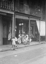 Women and children standing on a covered sidewalk, New Orleans, between 1920 and 1926. Creator: Arnold Genthe.