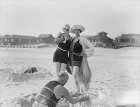 Unidentified man building sand castle and two women, Long Beach, New York, between 1911 and 1942. Creator: Arnold Genthe.