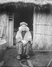 Ainu woman seated in front of the doorway of a hut, 1908. Creator: Arnold Genthe.