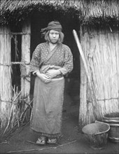 Ainu woman standing by the doorway of a hut, 1908. Creator: Arnold Genthe.