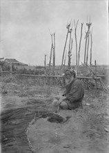Seated Ainu man working on fishing nets, 1908. Creator: Arnold Genthe.