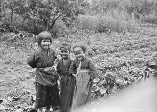 Three Ainu children standing in a garden, 1908. Creator: Arnold Genthe.