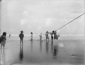 Children swinging on pier rope at beach, between 1900 and 1910. Creator: Unknown.
