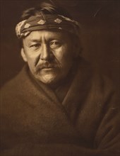 A Navajo man, head-and-shoulders portrait, wearing blanket and headband, facing front, c1904. Creator: Edward Sheriff Curtis.