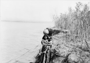 Mohave woman carrying water on her head and holding child, c1903. Creator: Edward Sheriff Curtis.