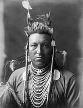 Swallow Bird, Crow Indian, Montana, head-and-shoulders portrait, facing front, painted..., c1908. Creator: Edward Sheriff Curtis.