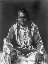 Wades in Water, Piegan Indian, full-length portrait, seated on floor, facing front..., c1910. Creator: Edward Sheriff Curtis.