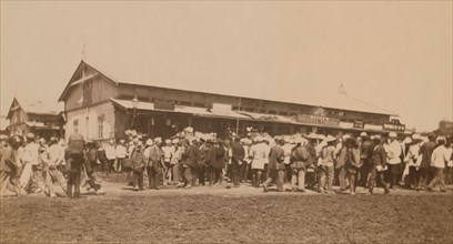 Crowds of people in front of buildings at the marketplace in the center of town..., (1899?). Creator: Eleanor Lord Pray.