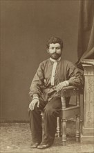 Full-length portrait of Armenian man, seated, facing front, between 1870 and 1886. Creator: Unknown.