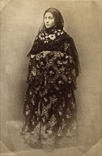 Full-length portrait of a woman in traditional dress, facing slightly left, between 1870 and 1886. Creator: Unknown.