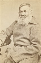 Three-quarter length portrait of an elderly convict, facing slightly left, between 1880 and 1886. Creator: Unknown.