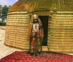 Woman in traditional dress and jewelry standing on rug in front of yurt, between 1905 and 1915. Creator: Sergey Mikhaylovich Prokudin-Gorsky.