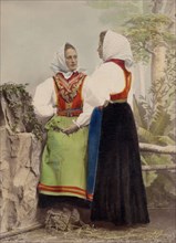 Two young women pose in folk costumes, with dotted headdresses, 1886-1890. Creator: Helene Edlund.