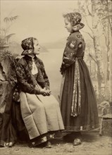 Two young girls pose in costumes from Dala-Floda with floral jackets and hats, 1890-1900. Creator: Helene Edlund.