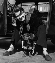 Photographer Kerstin Bernhard sits in the doorway of her car and holds a dachshund, 1955-1960. Creator: Unknown.