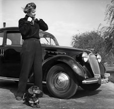 Photographer Kerstin Bernhard stands next to a car with her dachshund, 1955-1960. Creator: Unknown.