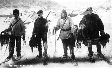 Kamchadal hunters against the backdrop of the city, with guns, furs, on skis, 1910-1929. Creator: Ivan Emelianovich Larin.