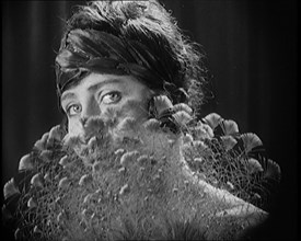 Female Civilian Wearing a Headband Hiding Her Face Behind a Feathers Fan, 1920. Creator: British Pathe Ltd.