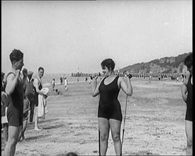 Female Civilian Wearing a Swimsuit Exercising with Elastic Bands on a Beach, 1920. Creator: British Pathe Ltd.