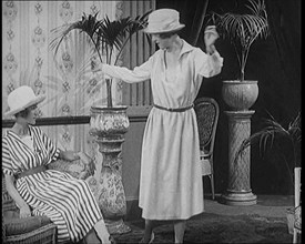 Two Female Civilians Leisuring in a Drawing Room Wearing Long Dresses and Hats Comparing..., 1920. Creator: British Pathe Ltd.