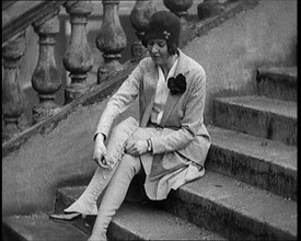 Female Civilian Doing up the Buttons of Her Leather Boots Sitting on Steps Outdoors, 1920. Creator: British Pathe Ltd.