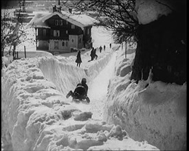 A Female Civilian Sledging down a Snowy Track Watched by Other Civilians with a Picturesque..., 1920 Creator: British Pathe Ltd.