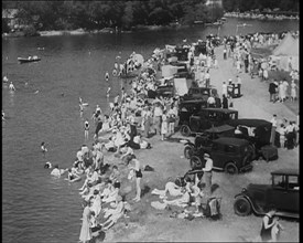 Large Group of People Sitting by a Riverside with Cars, 1933. Creator: British Pathe Ltd.