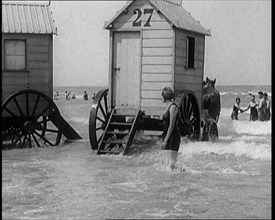 Female Civilian in Bathing Suit Standing in the Sea Watching Changing Cabins on Wheels Being...,1924 Creator: British Pathe Ltd.