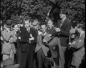 A Group of Male Civilians and One Soldier Listen to a Man With a Cigarette Standing on a..., 1938. Creator: British Pathe Ltd.