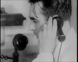 A British Man Holding a Candlestick Telephone Receiver to His Ear and Speaking Into the..., 1939. Creator: British Pathe Ltd.