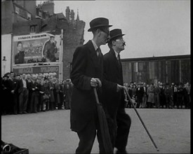 Two British Men in Suits and Hats Dancing in a Square With Men and Woman Watching Them..., 1938. Creator: British Pathe Ltd.