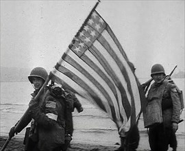 An American Soldier Holding an American Flag on a North African Beach as Part of 'Operation...1942. Creator: British Pathe Ltd.