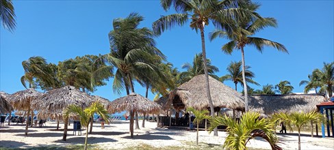 Thatched umbrellas and restaurant at the beach resort of Playa Ancon, south of Trinidad, Cuba, 2024. Creator: Ethel Davies.