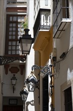 Narrow street with old lamps and balconies in the pedestrian area of Seville, Spain, 2023. Creator: Ethel Davies.