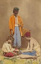 Unidentified man with basket standing, plus two boys seated playing cards, 1865-1870. Creator: Giorgio Conrad.