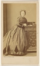 Unidentified woman standing, leaning against a credenza, about 1861. Creator: Bayard & Bertall.