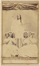 Female group portrait, six in white gowns kneeling, one standing holding a cross, about 1865. Creator: Unknown.