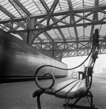 Looking along a bench with curved wrought iron arms on a platform at Waterloo Station with a train
