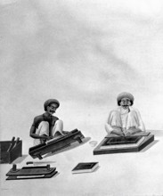 Two Indian bookbinders: one trimming page edges in a press, the other decorating a binding. Creator: Unknown.