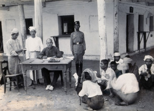 A man sitting at a table examining passports, during a plague epidemic in Mandalay, 1906. Creator: Unknown.