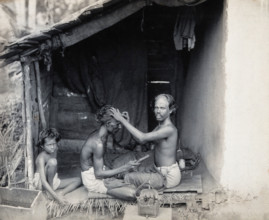 Two men sitting cross-legged; one is a barber shaving the front of the other's head, c1900. Creator: Unknown.