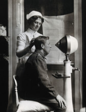 A young uniformed man sitting with a pillow on his chair, facing a machine..., c1910s. Creator: Unknown.