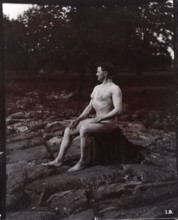 A man posing naked, seated on a rocky outcrop in a leafy landscape, c1900. Creator: Unknown.