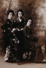 Three young women posing in a photographic studio, one seated on a bench..., early 20th century. Creator: Unknown.