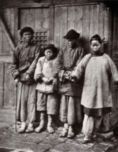 Foochow, China: four people with leprosy, wearing thick clothing, standing outside a wooden..., 1873 Creator: John Thomson.