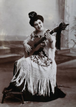 A seated woman, playing a guitar, wearing a fringed shawl, c1900. Creator: Unknown.