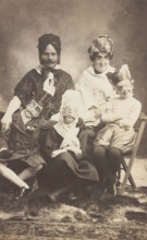 A family, all members wearing grotesque masks, the father in drag, c1910. Creator: Unknown.