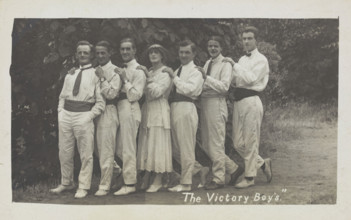 Entertainers, one in drag, pose in a line in front of foliage, [between 1910 and 1919?]. Creator: Unknown.